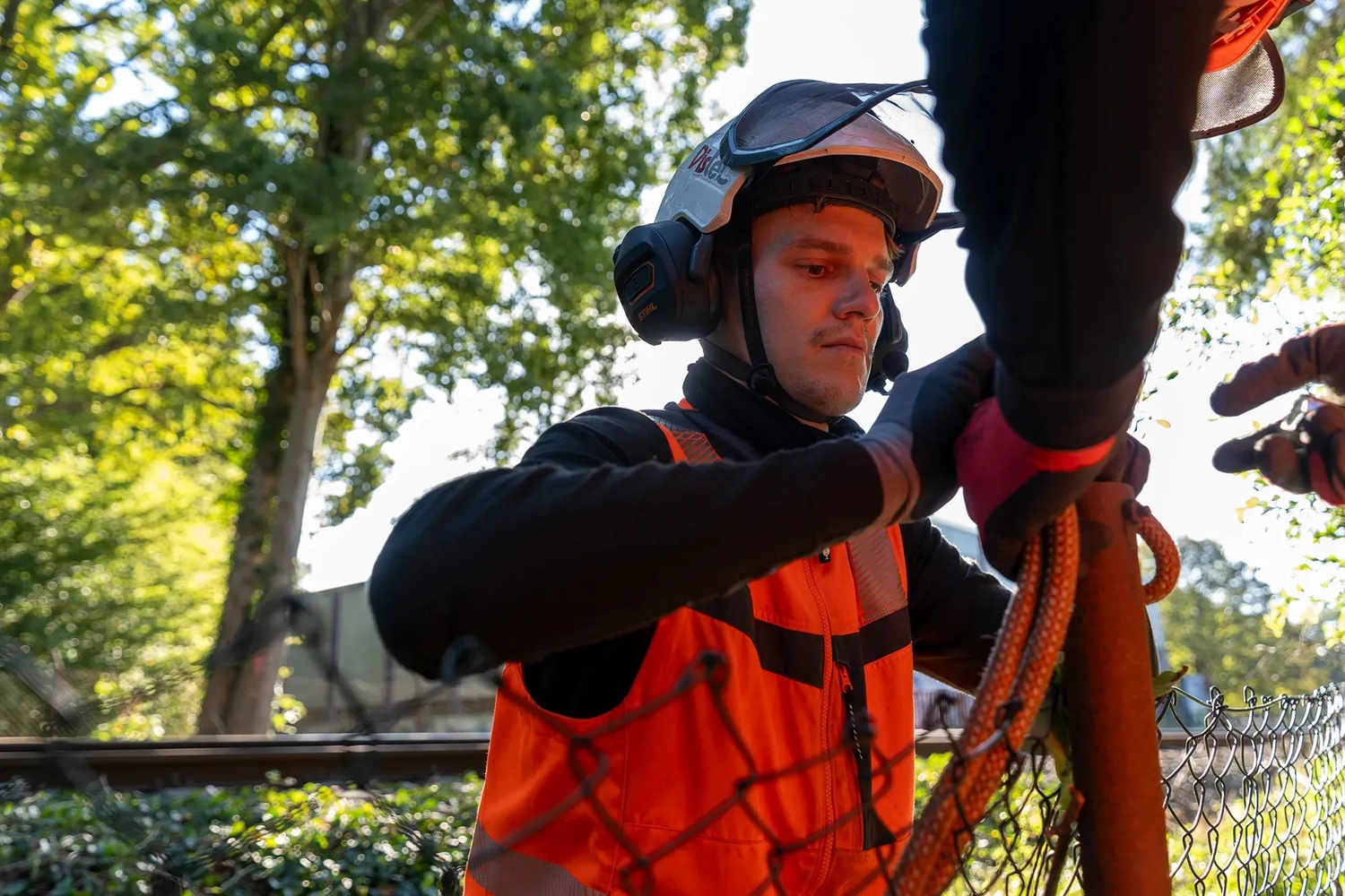 rundum baum GmbH - Baumpflege - Nahaufnahme eines Arbeiters, der schwere Seile und Anschlagmittel auf einer Baustelle justiert.